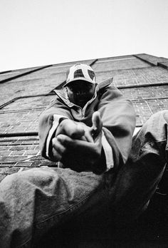 black and white photograph of a man sitting on the side of a building with his feet up