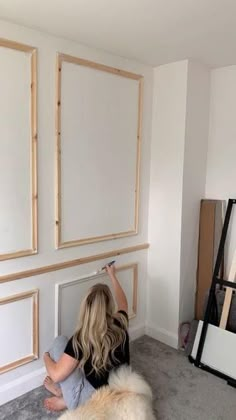 a woman is sitting on the floor in front of some framed pictures and holding a paintbrush