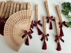 several wooden fans with tassels and bows are arranged on a white surface next to green leaves