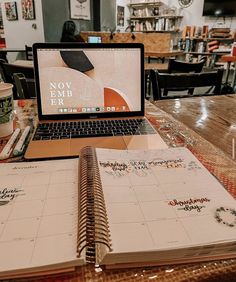 a laptop computer sitting on top of a wooden table next to a notebook and coffee cup