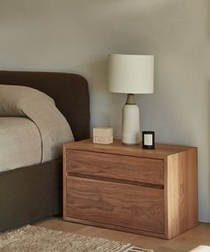 a nightstand with a lamp on top of it next to a bed