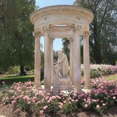 the statue is surrounded by pink flowers and greenery in front of a gazebo