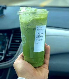 a hand holding up a green drink in a cup with a sticker on it