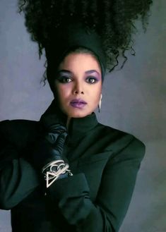 a woman with an afro is posing for the camera, wearing black gloves and holding her hand on her shoulder