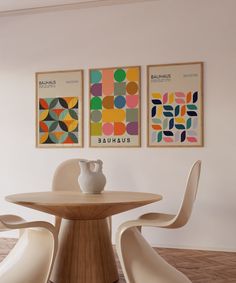 two paintings hang on the wall next to a table with chairs and vase in front of it