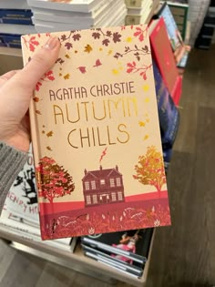 a person holding up a book in front of bookshelves with fall leaves on them