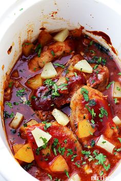 a white bowl filled with meat and vegetables covered in sauce, garnished with parsley