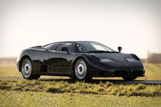 a black sports car driving down a road next to a lush green field with tall grass