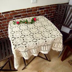 a table with two chairs and a white crocheted tablecloth on it next to a brick wall