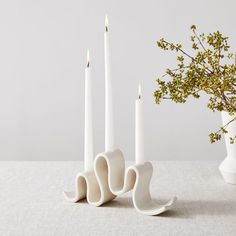 three white candles sitting on top of a table next to a vase filled with flowers