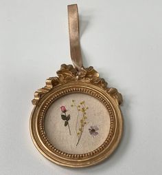 a gold frame with flowers on it hanging from a ribbon attached to a wall ornament