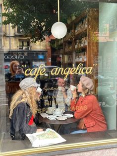 two women sitting at a table in front of a cafe window talking to each other