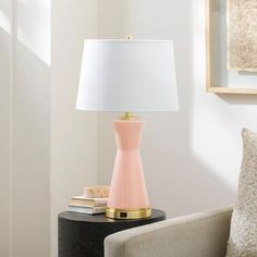 a pink lamp sitting on top of a table next to a white pillow and chair