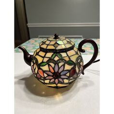 a stained glass teapot sitting on top of a white table next to a wall