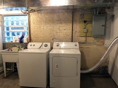 two washers and a dryer in a room with exposed pipes on the wall