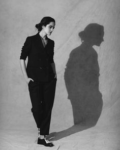 a woman standing in front of a white wall with her shadow on the wall behind her