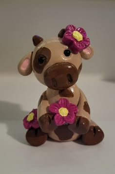 a brown and white cow figurine with pink flowers on its head sitting down