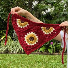 a woman holding up a red crocheted triangle with sunflowers on it