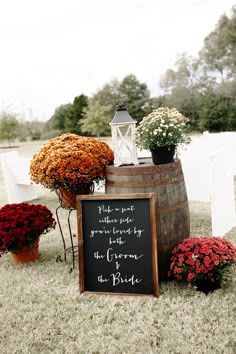 a chalkboard sign sitting on top of a barrel filled with red and orange flowers