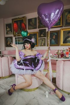 a woman sitting on top of a pink chair holding a purple heart shaped balloon in her hand