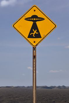 a yellow sign that is on top of a pole in the grass with mountains in the background