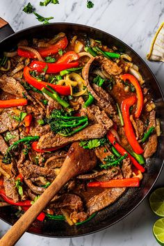 a skillet filled with beef, peppers and broccoli next to sliced limes