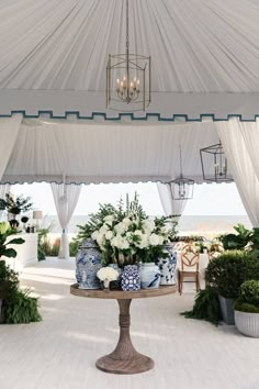 a table topped with vases filled with flowers under a white tent covered by curtains