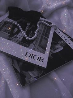 two dior necklaces are laying on top of a white sheet with sparkling lights