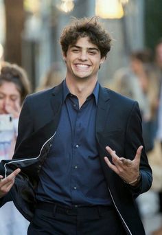 a man in a suit is smiling and holding his hands out while walking down the street