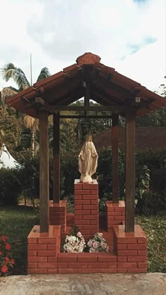 a statue in the middle of a brick structure with flowers around it and a gazebo