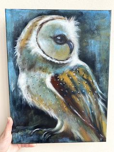 a painting of an owl is being held up by a person's hand in front of it