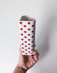 a woman's hand holding a white vase with red hearts on the outside and inside