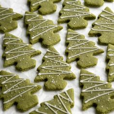 green cookies decorated with white icing are on a sheet of parchment paper and ready to be cut into christmas trees