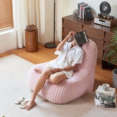 a woman sitting on a pink bean bag chair in her living room reading a book