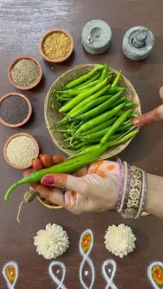 a person holding a bunch of green beans in front of some bowls and spoons