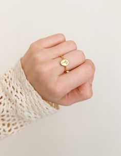 a woman's hand wearing a gold ring with a small heart on the middle