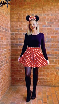 a woman wearing minnie mouse ears and a red polka dot skirt is standing in front of a brick wall