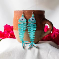 a cup with some beads hanging from it's side next to a flower pot