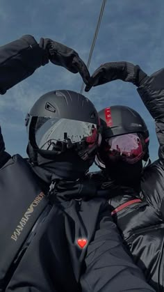 two people in black jackets and helmets holding their hands together