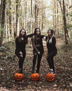 three young women in black outfits posing with pumpkins