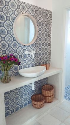 a white sink sitting under a bathroom mirror next to a vase with flowers in it