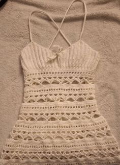 a white crocheted dress laying on top of a bed next to a pillow