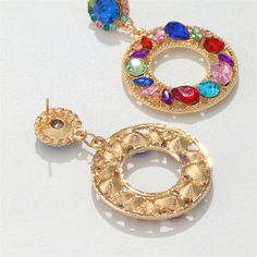 Eye-catching round drop earrings featuring multi-color crystal and cubic zirconia set in an 18k gold-plated finish. 1.26" W x 2" L 18k gold-plated copper / crystal / cubic zirconia Gold Jeweled Crystal Earrings, Jeweled Round Metal Earrings, Jeweled Round Crystal Earrings, Gold Jeweled Round Earrings, Multicolor Jeweled Round Earrings, Gold Crystal Round Earrings, Copper Crystal, Color Crystal, Blue Crystals