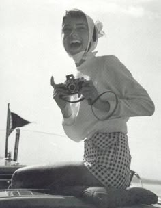 a woman sitting on the back of a boat holding a camera and making a funny face