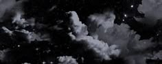 black and white photograph of clouds in the night sky, with stars above them as well