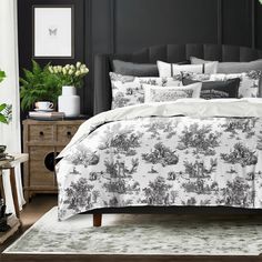 a bed with black and white comforters in a room next to a dresser, potted plant and mirror