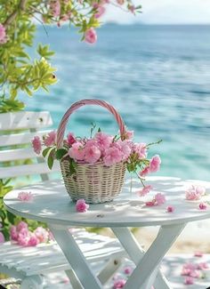 a basket with pink flowers sitting on top of a white table next to the ocean