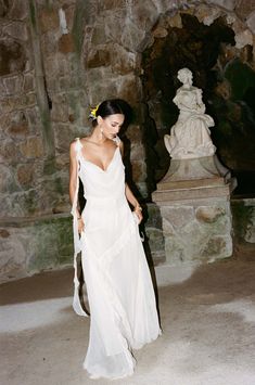 a woman in a white dress standing next to a stone wall