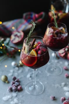 two glasses filled with red wine and garnished with rosemary, cranberries and orange slices