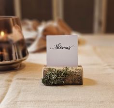 a place card holder with moss on it sitting on a table next to a candle